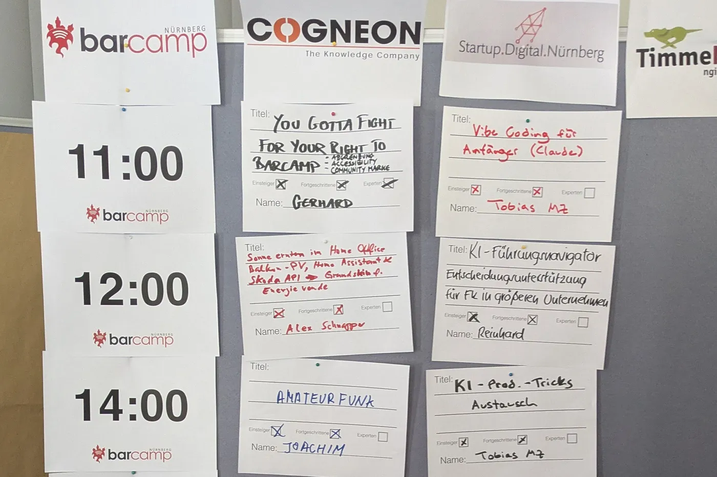 Sessionplan beim Barcamp Nürnberg: Pinnwand mit Uhrzeiten, Sponsorenlogos und handgeschriebenen Session-Zetteln, darunter Vibe Coding für Anfänger mit Claude und KI-Produktivitätstricks.